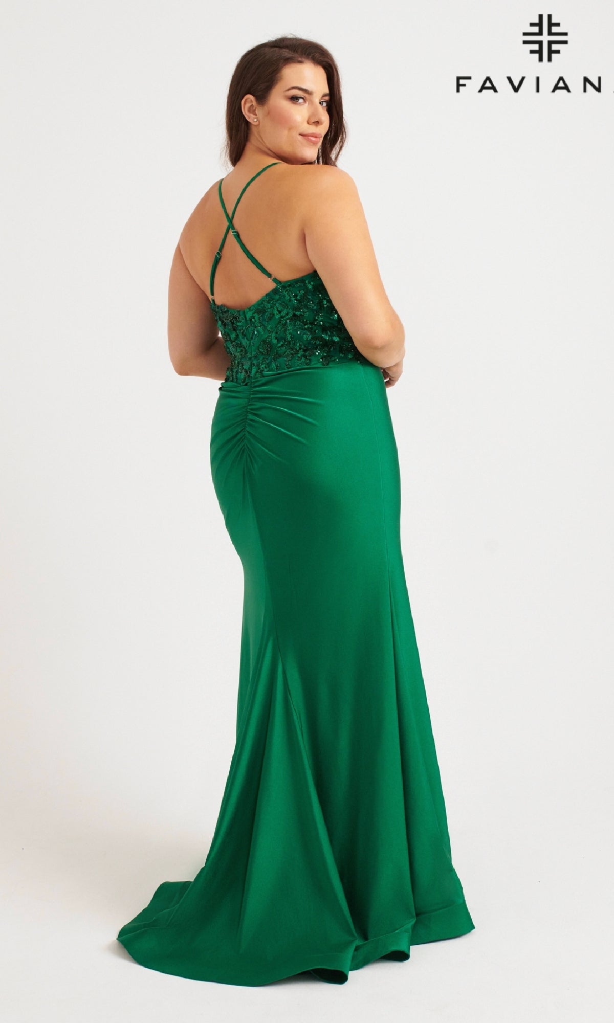 A woman in a green Plus-Size Strappy Long Prom Dress: Faviana 9570 poses with her back to the camera. This gown features a lace bodice, criss-cross straps, ruching at the back, sequin floral accents, and a floor-length skirt.